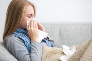 Close up of a young woman sneezing into a tissue.