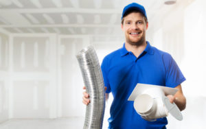 An HVAC technician holding up air duct parts.