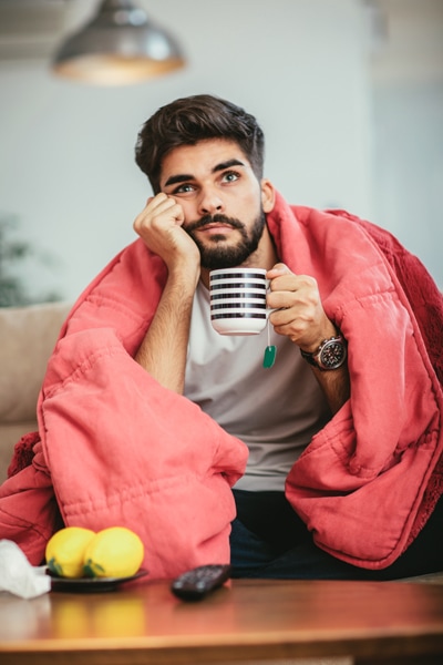 Man covered in a blanket drinking hot tea because his house is not warm.